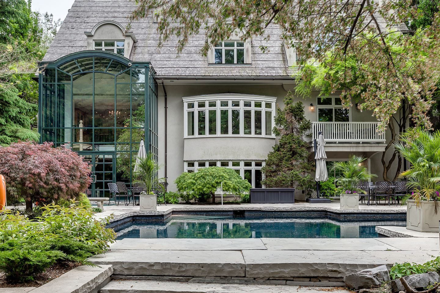 Luxury stone mansion exterior with glass conservatory and backyard pool